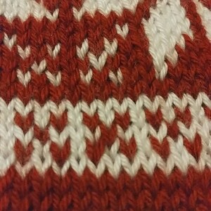 May include: Close-up of a knitted fabric with a red and white pattern. The fabric is made of yarn and has a textured surface.