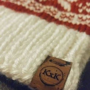 May include: White and red knitted hat with a brown leather tag that says "K.K.K."