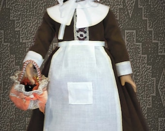 May include: A porcelain doll wearing a brown dress with a white apron and a white bonnet. The doll is holding a basket with a pink and white ribbon.