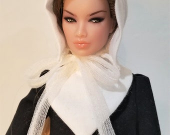 May include: A doll wearing a white bonnet and a black dress with white buttons. The doll has brown hair and brown eyes.