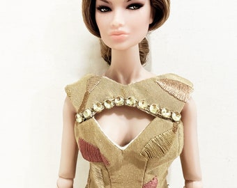 May include: A fashion doll with brown hair and a gold dress with a jeweled neckline and belt. The dress has a pink and gold pattern.