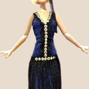May include: A doll with blonde hair wearing a black headband with a feather and a dark blue dress. The dress features a V-neckline, a vertical row of silver sequins, black lace trim, and a black fringe skirt that hangs from the waist.