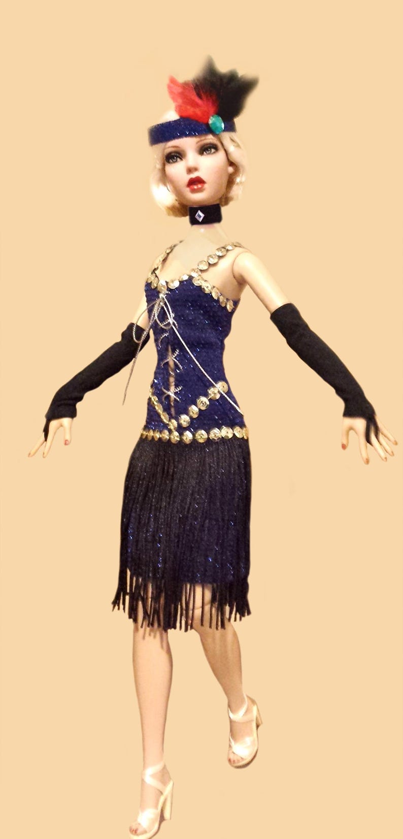 May include: A doll with blonde hair wearing a blue dress with gold sequins, a black fringe skirt, black opera gloves, a black choker, and a blue headband with red and black feathers. The doll wears white high-heeled sandals.
