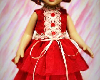 May include: A red dress with white lace trim and a red bow. The dress has a layered tulle skirt and is worn by a doll with brown hair and green eyes.