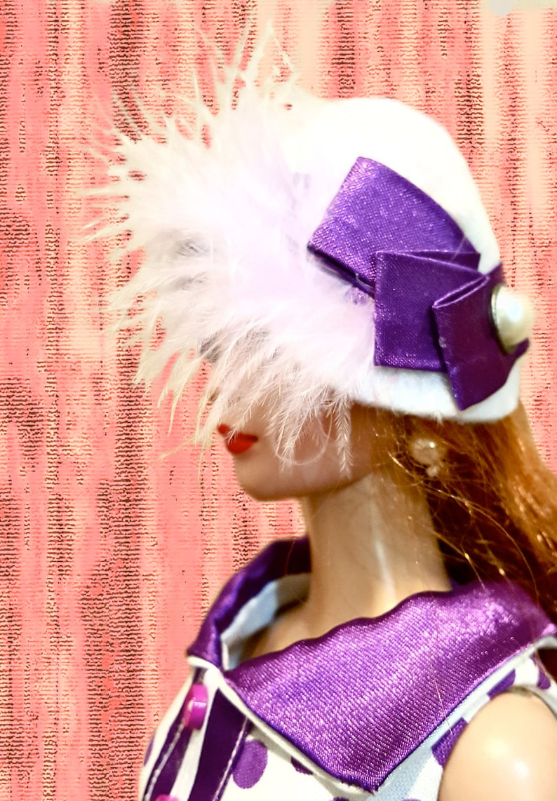 K&ouml;nnte beinhalten: Ein wei&szlig;er Hut mit einer gro&szlig;en violetten Satinschleife, einem wei&szlig;en Perlenakzent und hellrosa Federn. Der Hut wird zu einem wei&szlig;en Kleidungsst&uuml;ck mit violetten Punkten, einem violetten Kragen und einem passenden Knopf getragen.