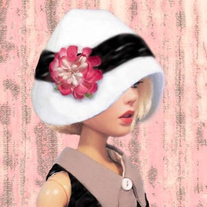 K&ouml;nnte beinhalten: Ein wei&szlig;er Glockenhut mit einem breiten schwarzen Band und einer gro&szlig;en, mehrlagigen rosa Stoffblume als Akzent. Der Hut wird von einer Puppe mit blondem Haar getragen, die ein schwarzes Kleidungsst&uuml;ck mit hellgrauem Kragen und wei&szlig;en Kn&ouml;pfen tr&auml;gt.