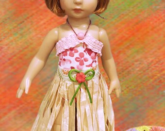 May include: A doll wearing a pink and white floral print dress with a straw grass skirt and a red flower headband. The doll has brown hair and blue eyes. The doll is standing on a wooden platform with a floral design.