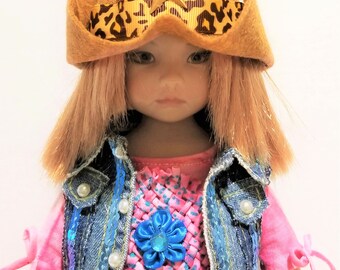May include: A doll wearing a brown felt cowboy hat with a leopard print band and gold star, a pink shirt with a blue flower, a denim vest with sequins, and a pair of denim shorts.