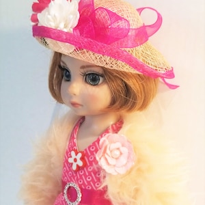 May include: A porcelain doll wearing a pink and white dress with a white fur jacket. The doll has blonde hair and is wearing a pink and white straw hat with a pink ribbon.