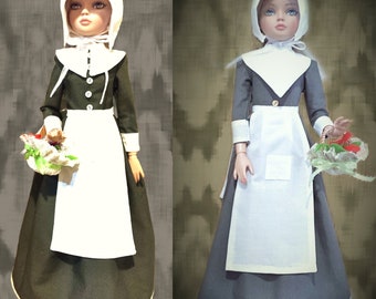May include: Two dolls dressed in pilgrim outfits with white bonnets, white collars, and white aprons over dark green dresses. Both dolls are holding baskets of flowers.