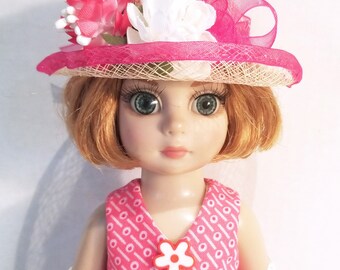 May include: A doll wearing a pink and white dress with a pink hat and white flowers. The doll has red hair and blue eyes.