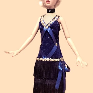 May include: A doll wearing a dark blue glittery dress with a V-neckline, silver sequin trim, and two tiers of black fringe. The doll has a black choker with a silver accent, a blue headband with silver sequins, and a red and black feather plume.