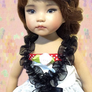 May include: A porcelain doll with brown hair wearing a white dress with black lace trim and a red and white polka dot bow headband.