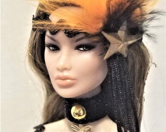May include: A doll with long brown hair wearing a black and gold sequined dress with a black velvet choker and a gold star and feather headband.