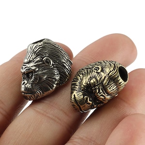 May include: Two silver and gold gorilla head keychains. The gorilla heads are detailed and realistic.