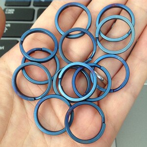 May include: A collection of blue metal split key rings. The rings are circular with a split opening for attaching keys or other items. The rings have a metallic sheen and are arranged in a pile.