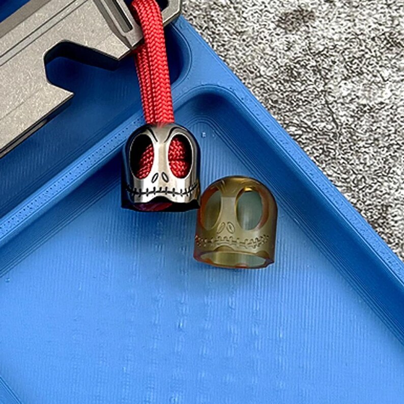 May include: Two skull-shaped keychains, one silver and one translucent amber, on a blue background.