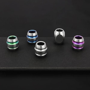 Puede incluir: Cinco cuentas de titanio en diferentes colores. Las cuentas son cilíndricas con un diseño acanalado. Los colores son azul, verde, morado y dos cuentas plateadas.