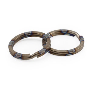 Op de afbeelding: Twee titanium sleutelringen met een blauw-bruine warmtebehandelde afwerking.
