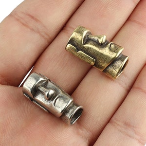 Peut inclure: Deux perles en métal en forme de visage, l'une argentée et l'autre en laiton, avec un design sculpté détaillé. Les perles mesurent environ 2,5 cm de long et sont parfaites pour ajouter une touche unique à des bijoux ou des porte-clés.