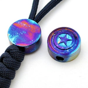 May include: Two round metal beads with a blue, purple, and orange iridescent finish. One bead has a star design inside a circle, the other is plain.