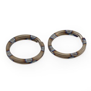 Op de afbeelding: Twee titanium sleutelringen met een blauwe en bruine iriserende afwerking. De ringen zijn dubbelwandig en hebben een glad, gepolijst oppervlak.