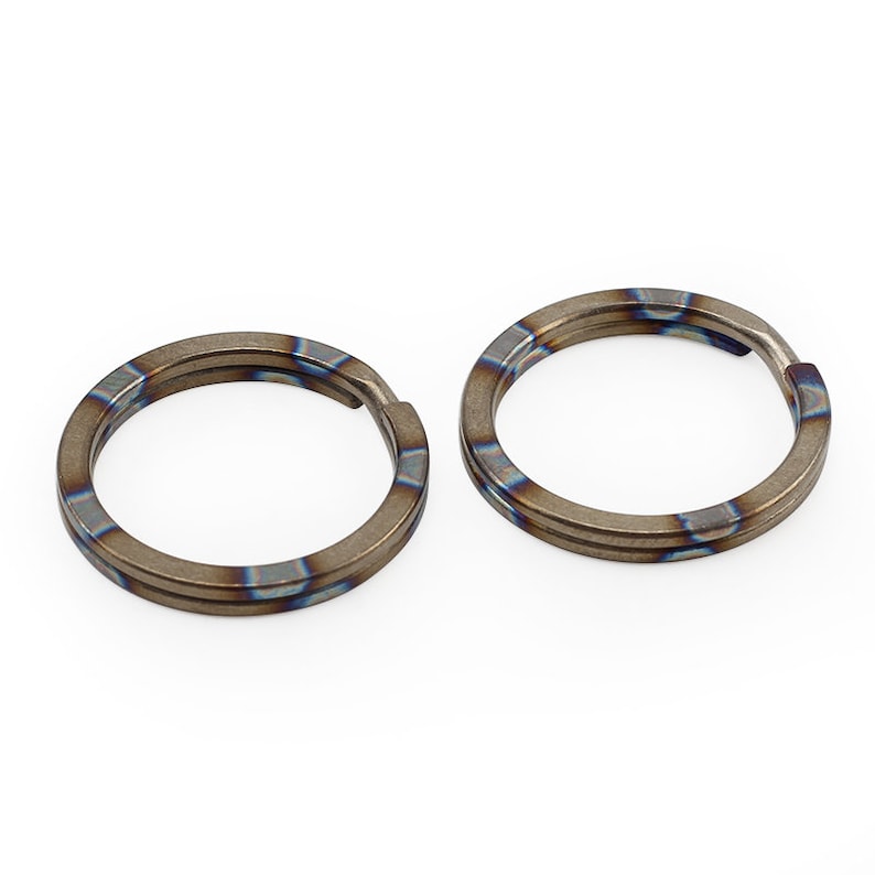Op de afbeelding: Twee titanium sleutelringen met een blauwe en bruine iriserende afwerking. De ringen zijn dubbelwandig en hebben een glad, gepolijst oppervlak.