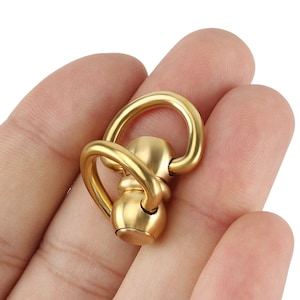 May include: A gold-toned metal swivel snap hook with a round, swiveling ball in the center. The hook is designed for attaching to keychains, bags, or other items.