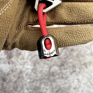 May include: A silver skull-shaped keychain with a red string attached. The skull has a stitched mouth and a black eye.