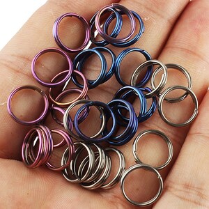 May include: A collection of colorful metal key rings in various shades of blue, purple, and silver. The key rings are arranged in a pile on a hand.
