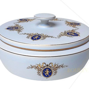 Könnte beinhalten: Eine weiße Keramik-Servierschüssel mit Deckel, mit goldenen Verzierungen und dekorativen blau-goldenen Medaillons mit Cherubfiguren. Die Schüssel hat eine runde Form und einen kleinen Griff auf dem Deckel.