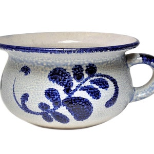 May include: A ceramic bowl with a handle, featuring a speckled, light gray base and a dark blue floral design. The rim and handle are also accented with dark blue. The bowl has a rounded shape.