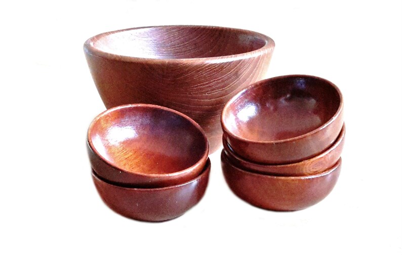 May include: A set of wooden bowls in varying sizes. The largest bowl is deep and round, while the smaller bowls are stacked in groups. The wood has a rich, reddish-brown color and a visible grain pattern, suggesting a natural finish.