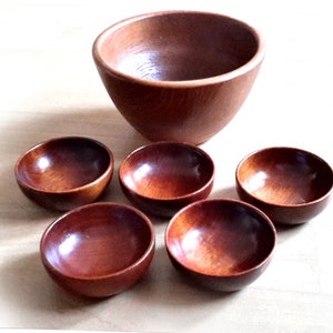 May include: A set of six wooden bowls. One large bowl is positioned above five smaller bowls. The bowls are made of a reddish-brown wood with a glossy finish. The bowls are empty and appear to be new.