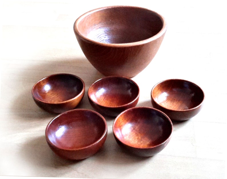 May include: A set of six wooden bowls. One large bowl is positioned above five smaller bowls. The bowls are made of a reddish-brown wood with a glossy finish. The bowls are empty and appear to be new.