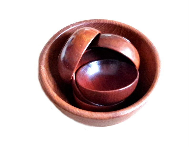 May include: A set of wooden bowls in varying sizes, nested within each other. The bowls are a warm, reddish-brown color, with a smooth, polished finish. The largest bowl is approximately 8 inches in diameter.