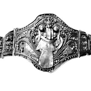 May include: An ornate silver belt with detailed patterns. The central section features a stylized face with a headdress, surrounded by floral and dot designs. The belt is segmented with connecting hinges.
