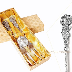 Può includere: Set di forchette da portata in argento vintage in una scatola decorativa. Le forchette presentano decorazioni floreali ornate sui manici e sono presentate in una scatola color oro con fodera in raso. La scatola è rettangolare e fantasia.
