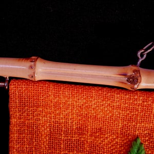 May include: Close-up of a bamboo rod with a metal chain and a hanging orange fabric. The bamboo rod has a natural, light brown color and is attached to the fabric with a metal hook. The fabric has a textured appearance.