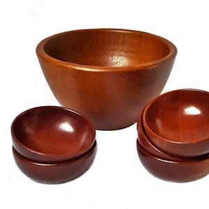 May include: A set of wooden bowls in varying sizes. The largest bowl is a light brown color, while the smaller bowls are a darker reddish-brown. The bowls have a smooth, polished finish, and are arranged on a white background.