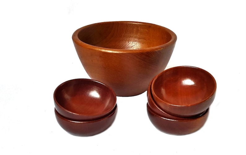 May include: A set of wooden bowls in varying sizes. The largest bowl is a light brown color, while the smaller bowls are a darker reddish-brown. The bowls have a smooth, polished finish, and are arranged on a white background.