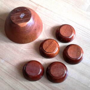 May include: A set of wooden bowls and coasters. The large bowl is a light brown color, and the coasters are a darker brown. The bowls and coasters are made of wood and have a smooth finish. The set is ideal for serving snacks or small dishes.
