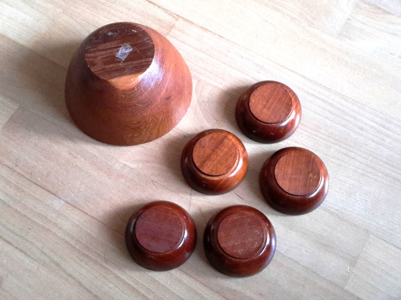 May include: A set of wooden bowls and coasters. The large bowl is a light brown color, and the coasters are a darker brown. The bowls and coasters are made of wood and have a smooth finish. The set is ideal for serving snacks or small dishes.