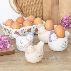 May include: A trio of cream-glazed ceramic mugs, each adorned with a hand-painted floral pattern in blue, green, and yellow. The mugs have a speckled finish and a classic, rounded design with a handle for easy grip.