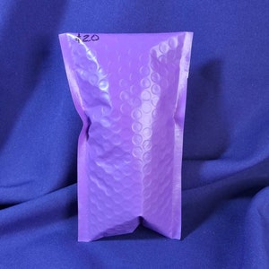 Puede incluir: Un sobre de burbujas lavanda peque&ntilde;o y sellado con un "$20" escrito a mano en tinta negra en la parte superior. El sobre est&aacute; hecho de un material texturizado y est&aacute; sobre un fondo azul.