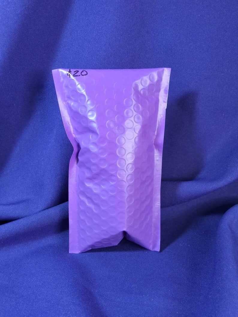 Puede incluir: Un sobre de burbujas lavanda peque&ntilde;o y sellado con un "$20" escrito a mano en tinta negra en la parte superior. El sobre est&aacute; hecho de un material texturizado y est&aacute; sobre un fondo azul.