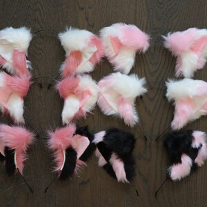Puede incluir: Un conjunto de diez diademas de orejas de gato de piel sint&eacute;tica. Las orejas son de color rosa y blanco, o negro y rosa. Las diademas son negras.