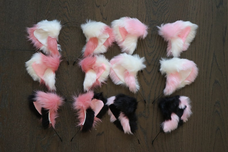 Puede incluir: Un conjunto de diez diademas de orejas de gato de piel sint&eacute;tica. Las orejas son de color rosa y blanco, o negro y rosa. Las diademas son negras.