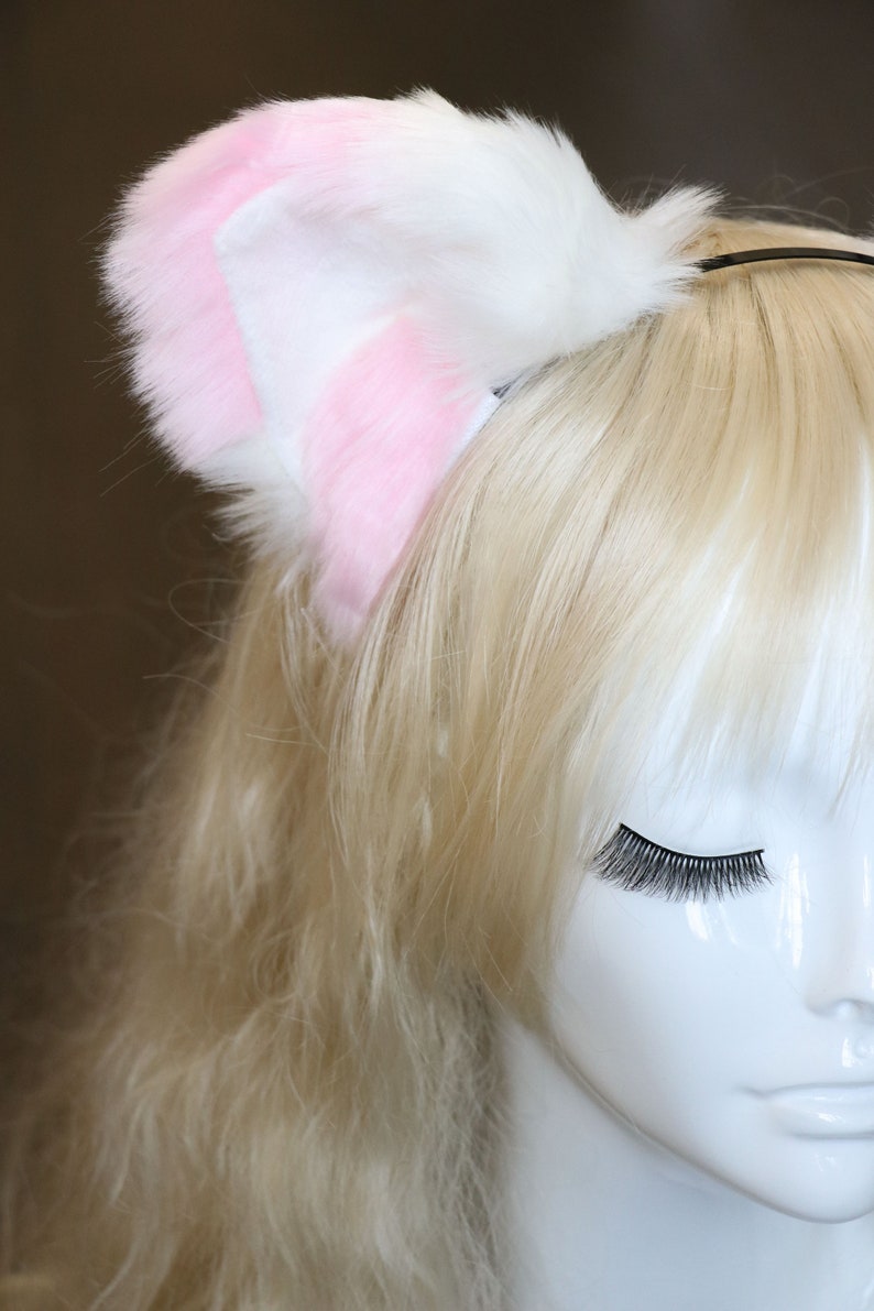 Puede incluir: Una diadema de orejas de gato de piel sint&eacute;tica blanca y rosa. La diadema se lleva en un maniqu&iacute; con el pelo largo y rubio.