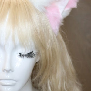 Puede incluir: Una cabeza de maniqu&iacute; blanca con cabello rubio que lleva una diadema de orejas de gato rosa y blanca.